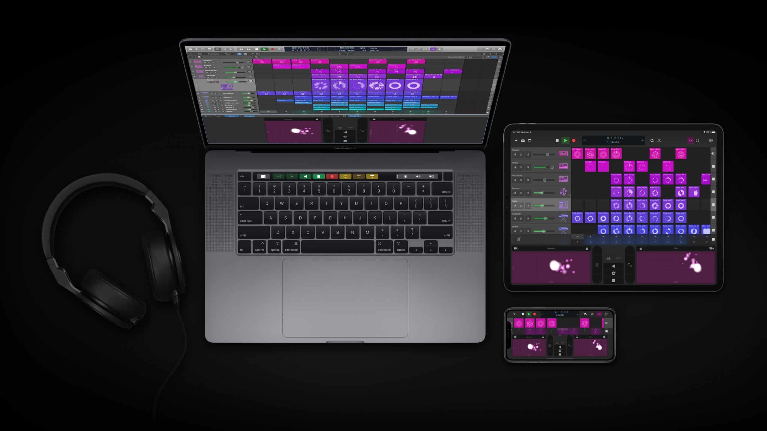 A laptop, tablet, and smartphone display music production software with similar colorful interfaces. The central laptop, running Logic Pro X after a recent software update, is flanked by the tablet and smartphone. A pair of Apple headphones is plugged into the laptop. All devices rest on a dark surface.