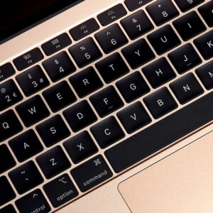 MacBook 12 Inch - Close-up of a gold MacBook keyboard with black backlit keys, showing the QWERTY layout and function keys.