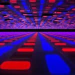 An abstract image featuring a grid of glowing red and blue rectangular blocks extends into the distance, creating a sense of depth and perspective. The colors are vibrant, evoking a futuristic digital aesthetic reminiscent of the latest screen technology found in Tandem OLED displays.