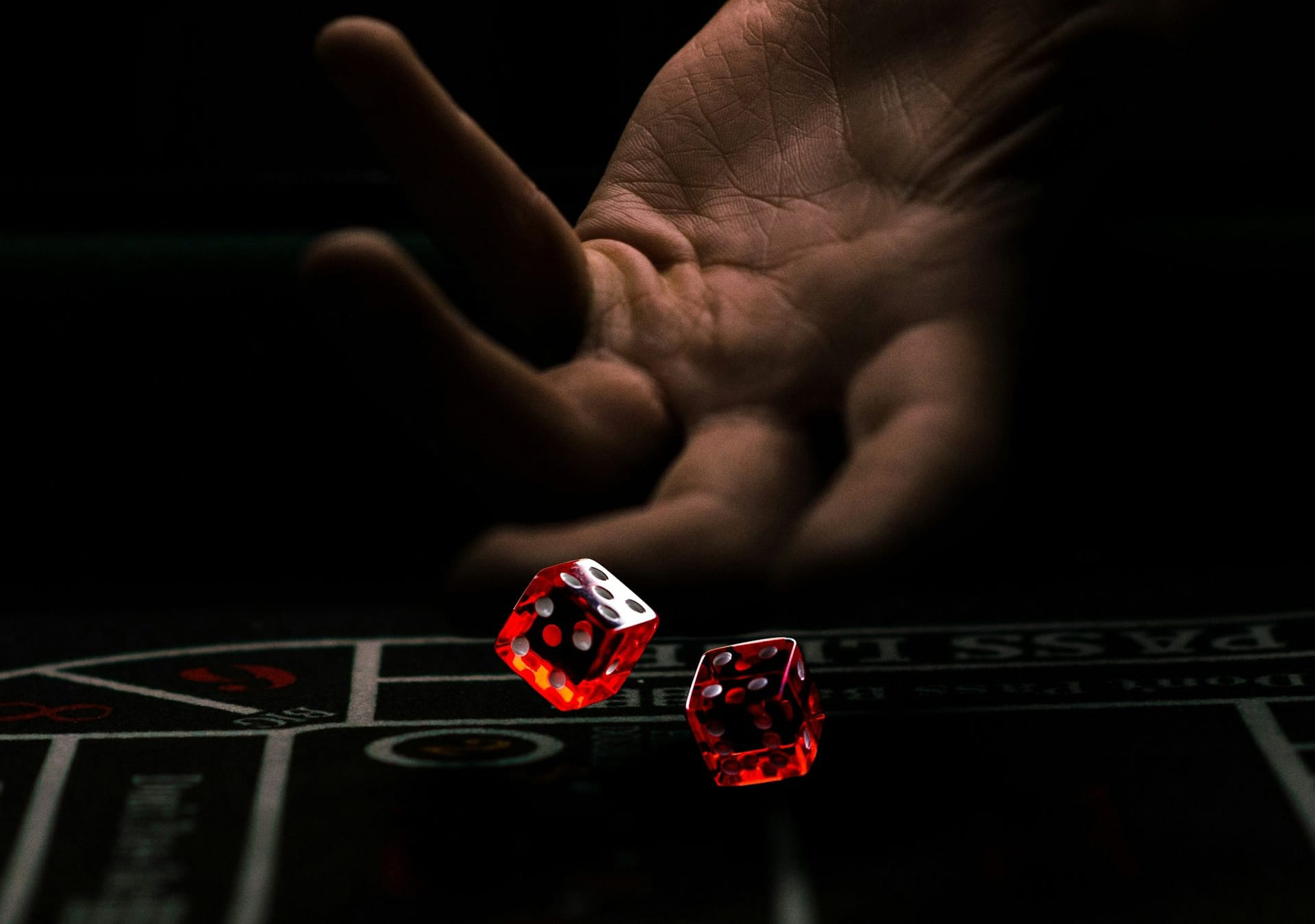A hand is captured in mid-motion, about to release two red dice onto a casino table. The background is dark, highlighting the illuminated dice and creating a dramatic atmosphere reminiscent of top entertainment apps.