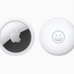 Two Apple AirTags rest on a white background. The left one proudly displays the iconic Apple logo surrounded by text, while the right features a charming smiley face. A small Apple logo graces the bottom corner, adding a touch of elegance to these innovative AirTags.
