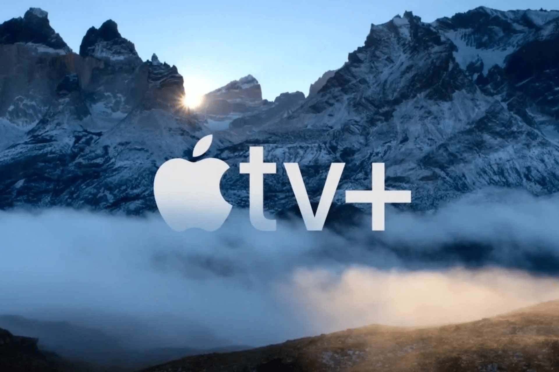 The Apple TV+ logo stands proudly against a majestic backdrop of rugged mountains, partially veiled in snow and mist. Sunlight peeks through the peaks, casting a serene and dramatic glow, perfectly mirroring the innovative spirit of Apple TV+.