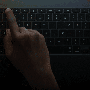 A hand with dark skin presses the escape key on a backlit laptop keyboard in a dimly lit environment, highlighting how essential shortcuts can boost productivity for iPad power users.