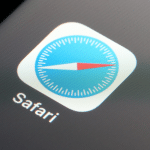 Close-up of the Safari web browser app icon on a device screen, featuring a blue compass with a red and white needle and the word "Safari" below it, highlighting its fresh look in iOS 26 with new features.