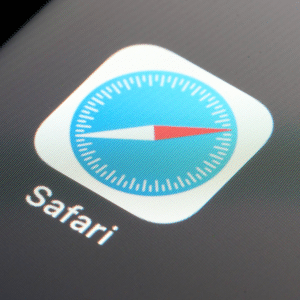 Close-up of the Safari web browser app icon on a device screen, featuring a blue compass with a red and white needle and the word "Safari" below it, highlighting its fresh look in iOS 26 with new features.
