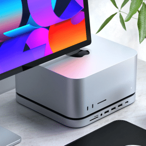 A close-up of a modern desktop setup featuring the new Mac Studio, a monitor with a colorful screen, a plant, and a cup of coffee on a white desk—perfect for ensuring a seamless transition when moving files between devices.