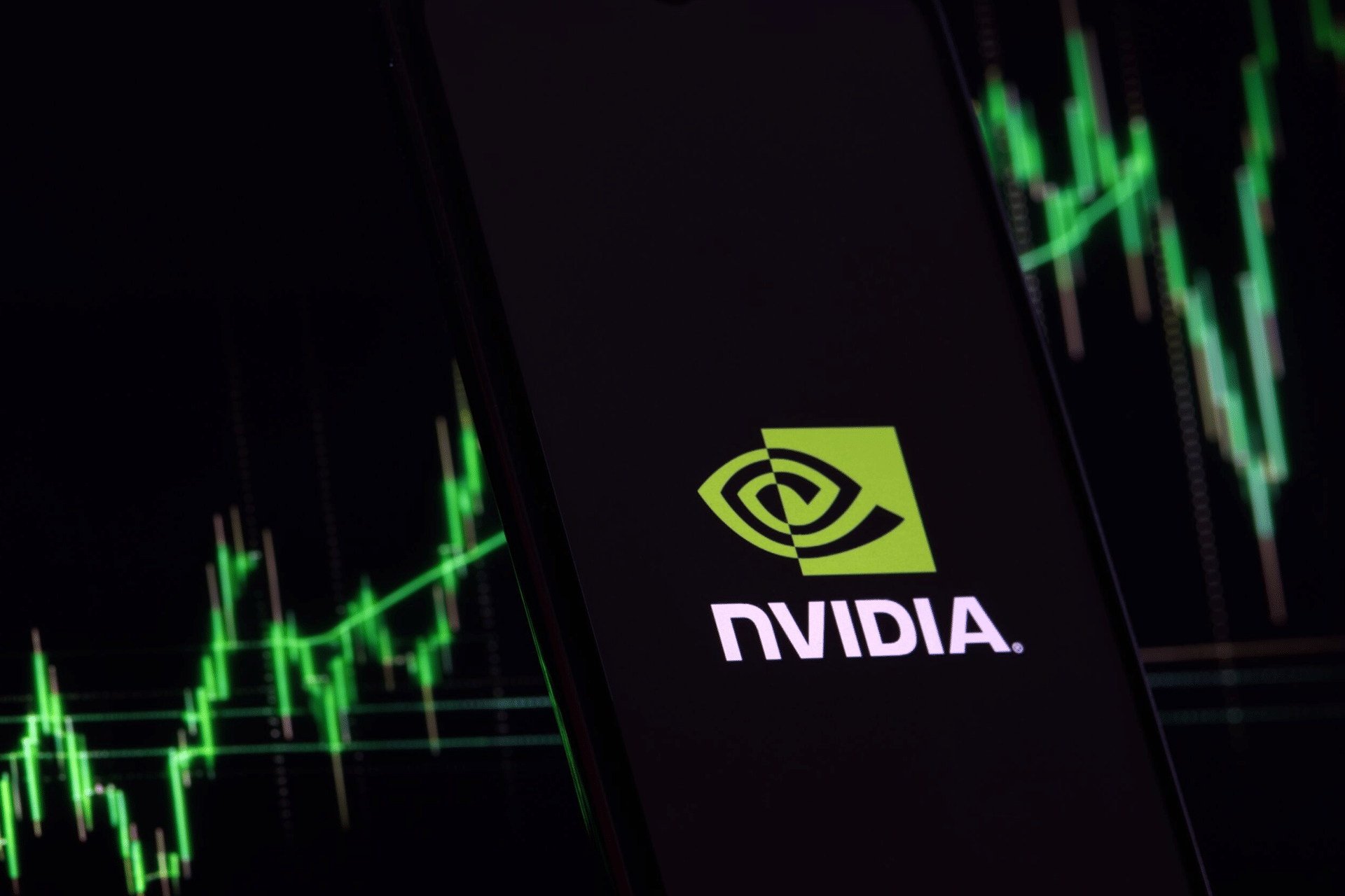 A smartphone displays the NVIDIA logo on a dark background, while a green upward-trending stock chart with candlestick patterns hints at AI-driven ETFs blurred in the background.