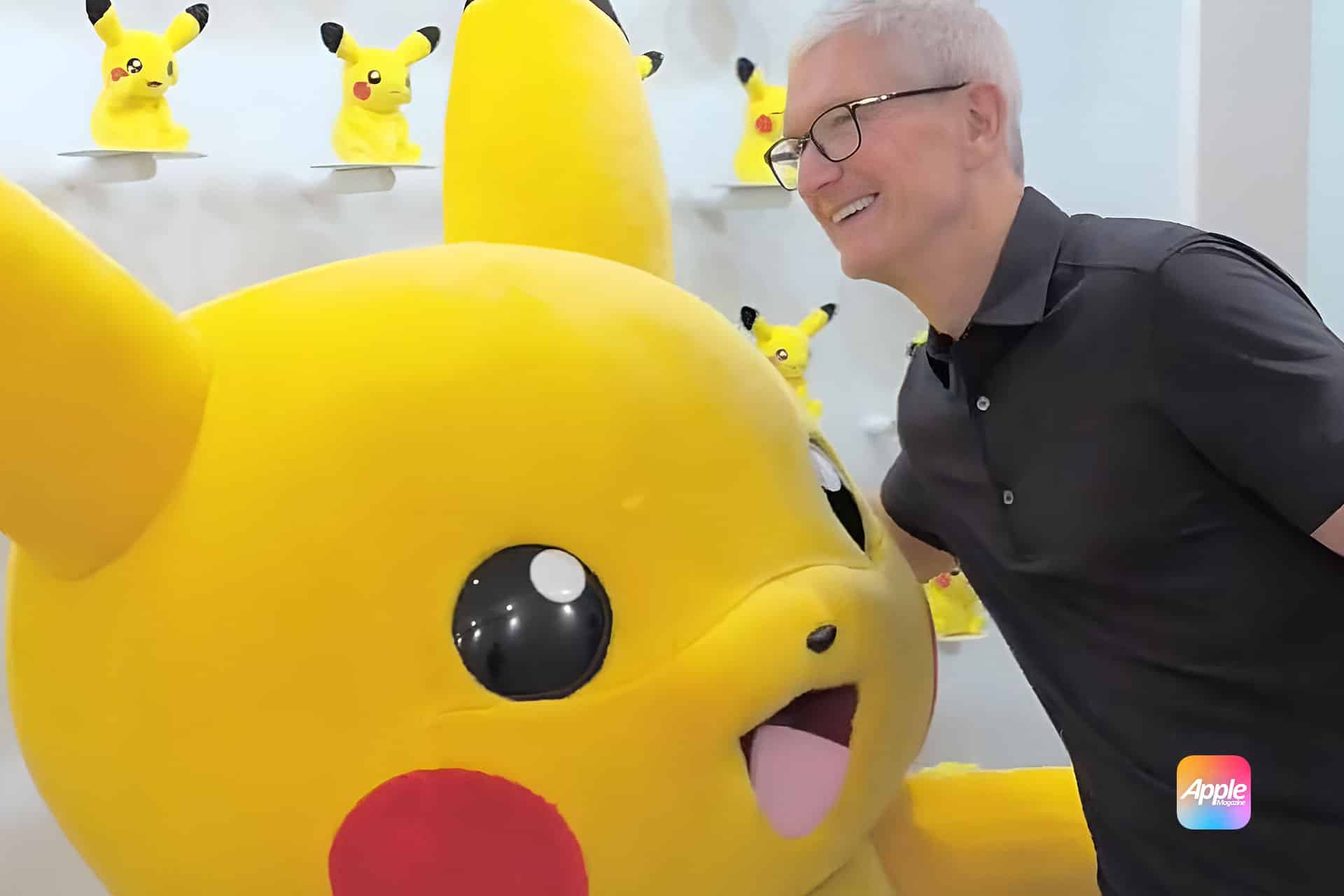 A man in a black shirt smiles while posing next to a large Pikachu mascot, with several smaller Pikachu figures on shelves in the background—capturing a true Tim Cook’s Pikachu Moment. An apple japanese logo is visible in the bottom right corner.