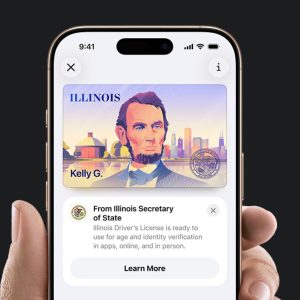 A hand holds a smartphone displaying an Illinois Digital ID in Apple Wallet, featuring Abraham Lincoln's portrait and the name "Kelly G." The screen also shows a notification about Illinois driver's license ID verification.