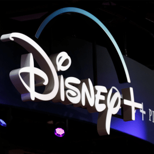 The Disney+ logo is illuminated on a dark background, with the Pixar and Marvel logos partially visible to the right. Purple and blue lights shine beneath the display, highlighting Disney Plus on older Apple devices.