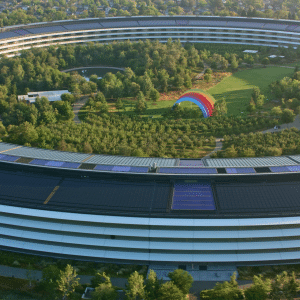 Aerial view of Apple Park, a circular building surrounded by trees, with a large colorful rainbow structure and green lawns inside the central courtyard—a testament to innovation fueled by notable Apple acquisitions.