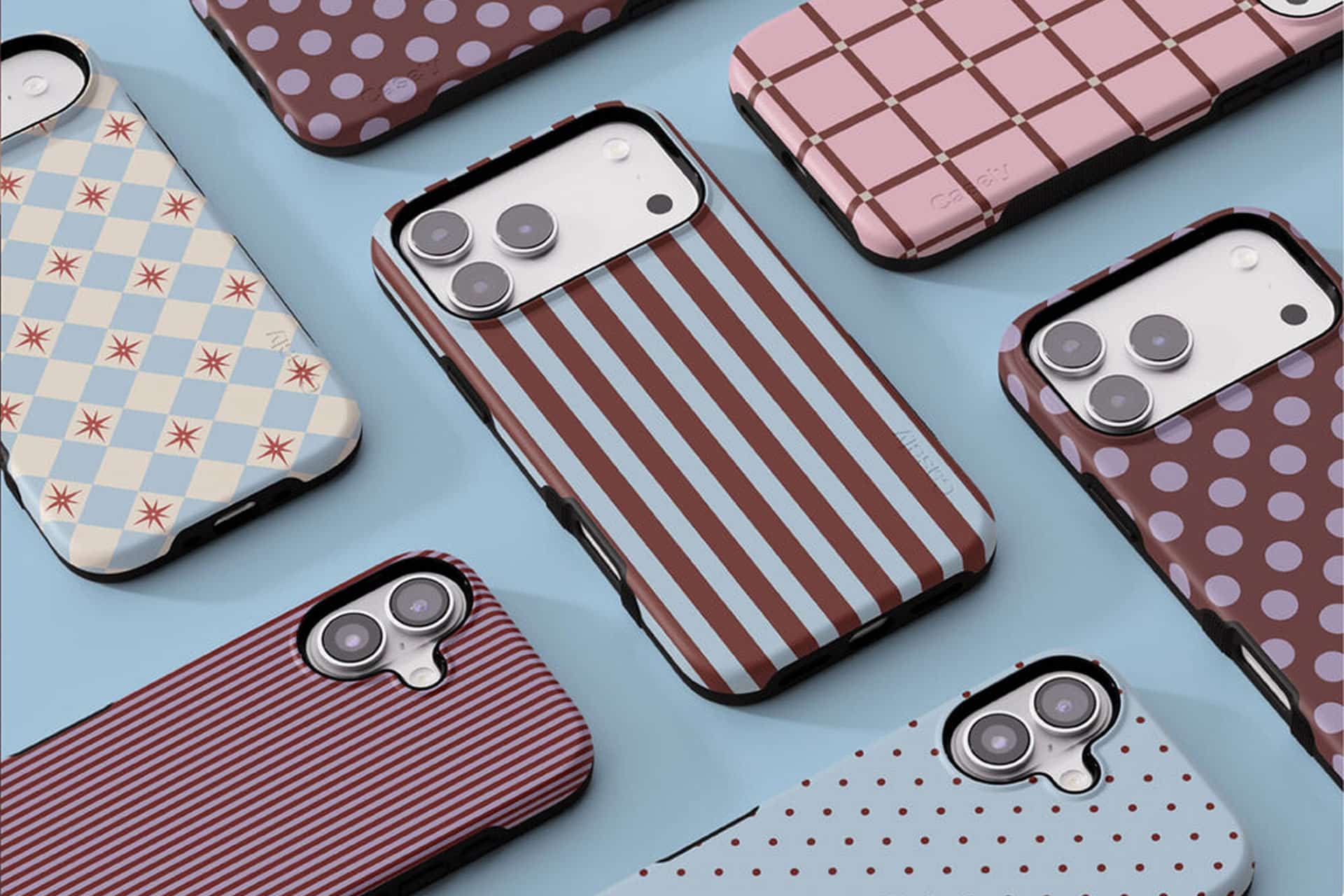 Several smartphones with camera lenses are placed on a blue surface, each featuring an iPhone case from popular iPhone case brands with colorful patterns like stripes, polka dots, grid lines, and geometric designs.