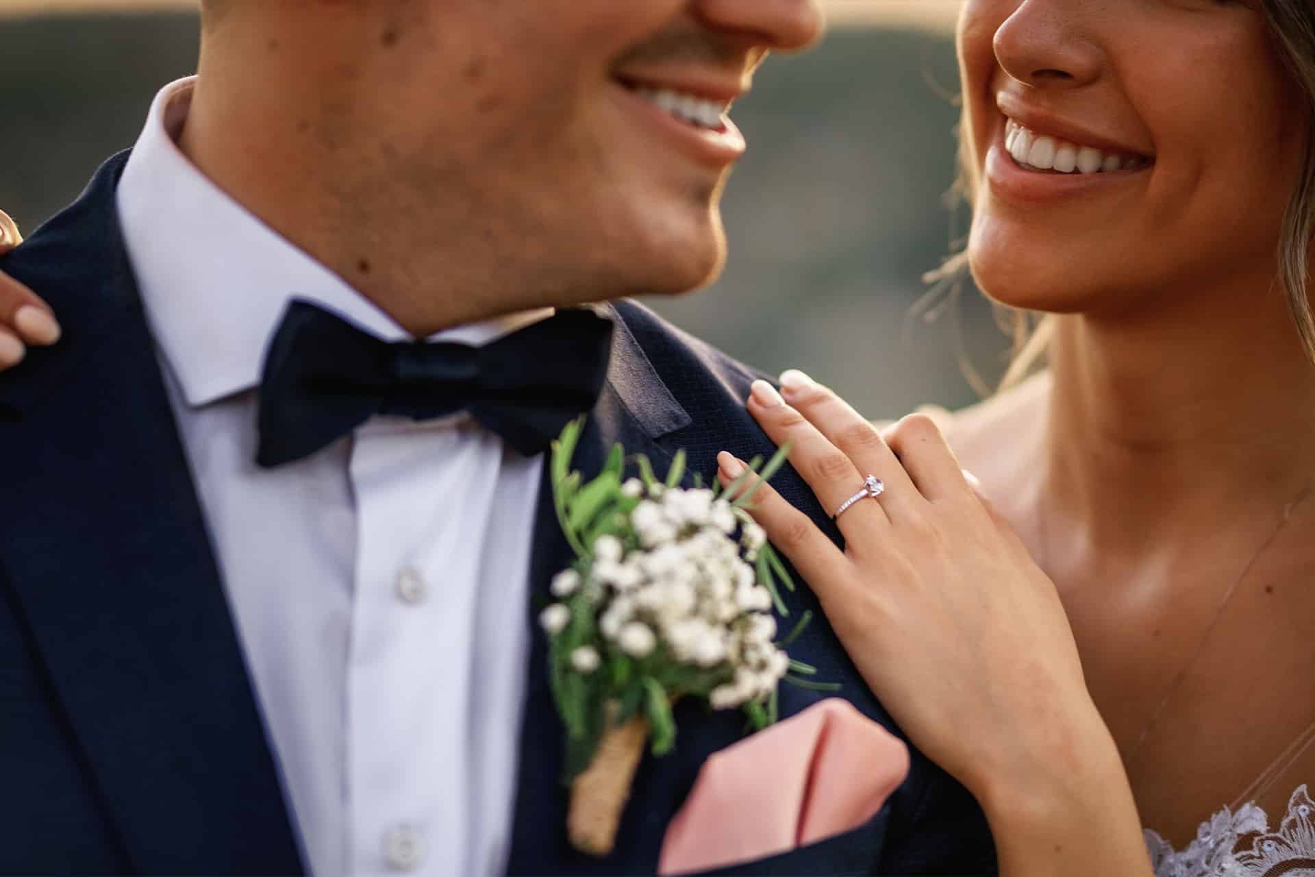 Close-up of engaged couple smiling with engagement ring visible during wedding celebration.