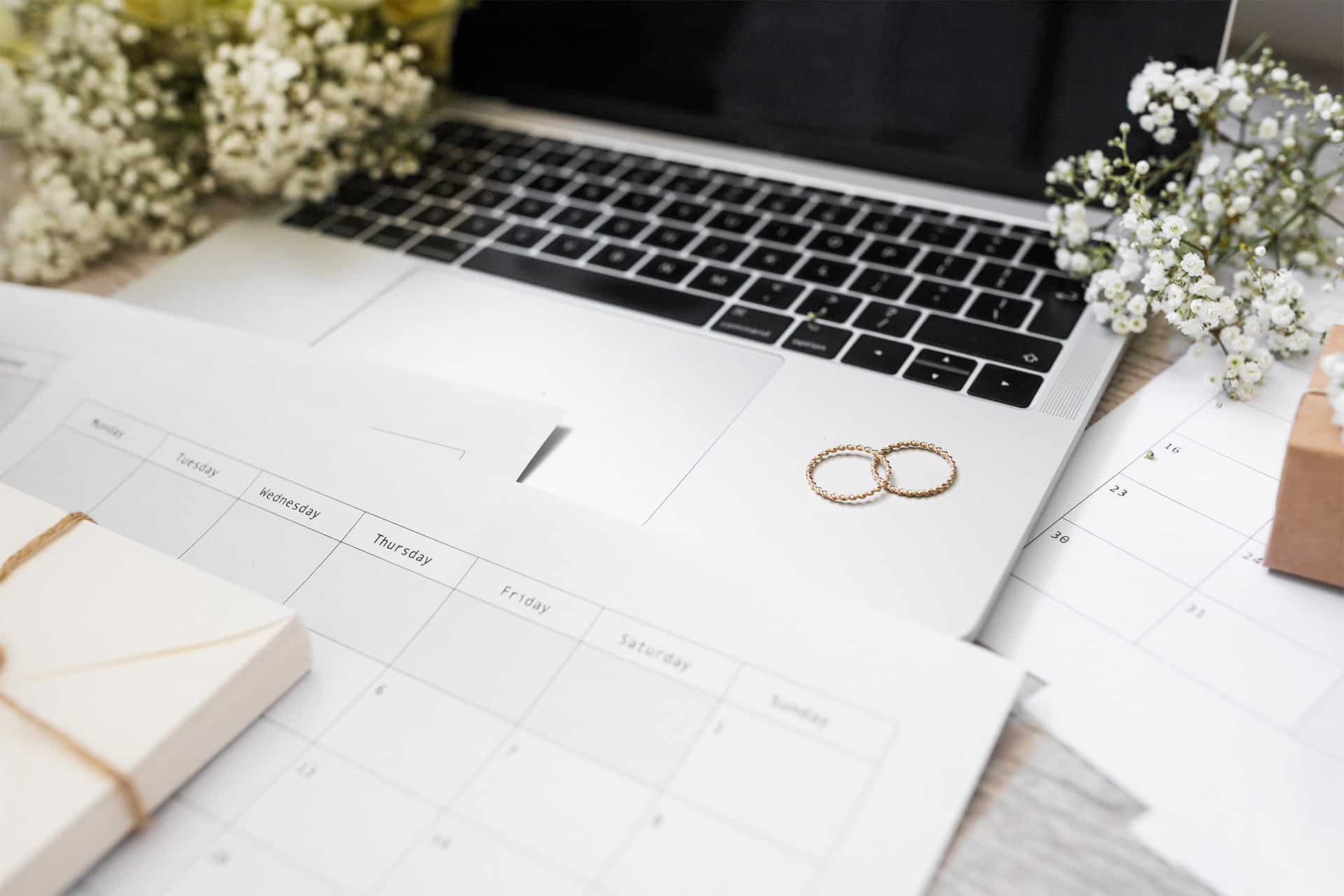 Wedding rings on a laptop keyboard with calendar and planning documents.