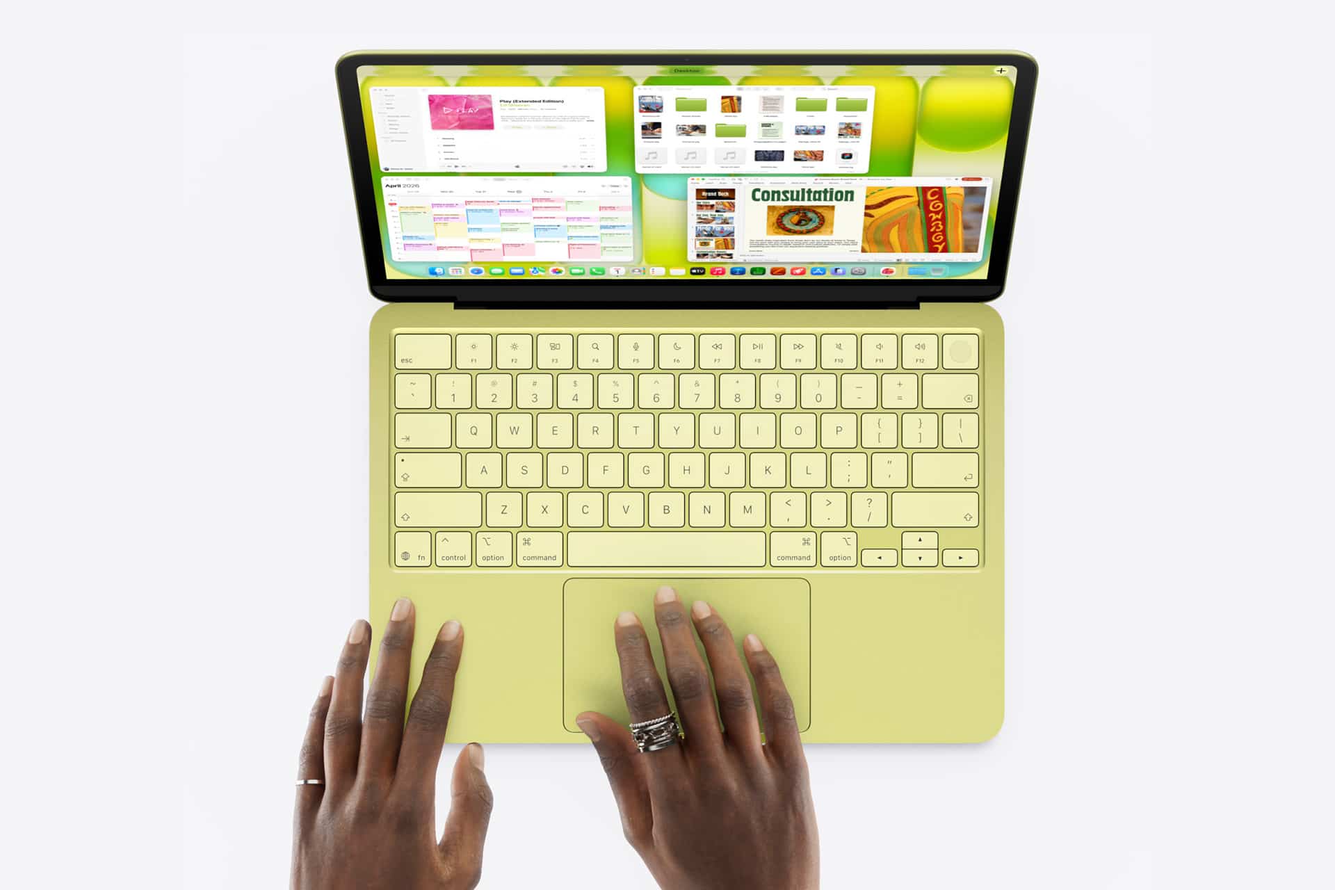 A person with rings on their fingers types on a yellow MacBook Neo, its screen displaying multiple open windows against a white background.