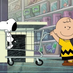 Charlie Brown pushes a shopping cart with Snoopy inside it through a store aisle filled with colorful products on shelves, capturing the heartwarming charm of a Peanuts special like those featured in "Snoopy Presents" on Apple TV.
