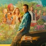 A man in a blue Hawaiian shirt leans against a car, holding a popsicle, with a colorful tropical mural behind him featuring various people and lush greenery—a scene reminiscent of the laid-back Florida vibes in Bill Lawrence’s Bad Monkey series on Apple TV.