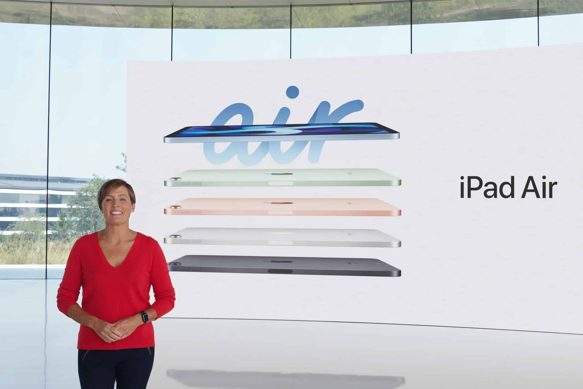 Laura Legros - A woman in a red sweater stands next to a large screen displaying five floating iPad Air tablets in different colors and the words “air” and “iPad Air,” highlighting Apple’s dedication to hardware engineering—a field led by innovators like John Ternus and Laura Legros.
