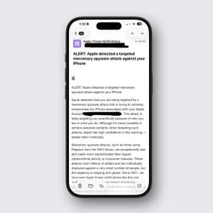 An iPhone displays an Apple notification email warning the user of a targeted mercenary spyware attack against their device. The email explains the threat, highlights Apple’s robust spyware warnings, and offers advice. The phone is shown on a light gray background.